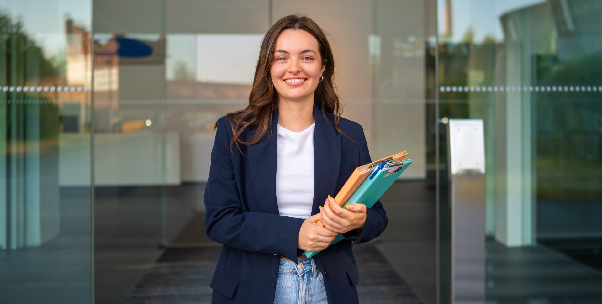 Jeune femme d'affaires, dossiers à la main, souriant à l'entrée du bureau