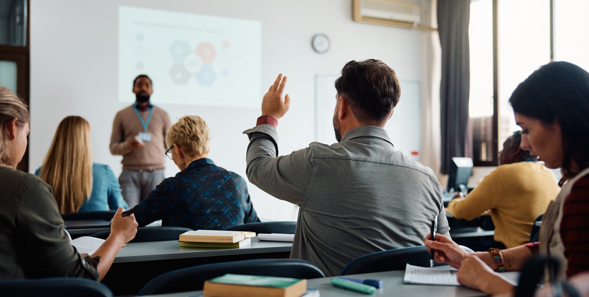 Vue de dos d'un étudiant plus âgé levant la main pour répondre à une question du professeur pendant un cours de formation pédagogique.